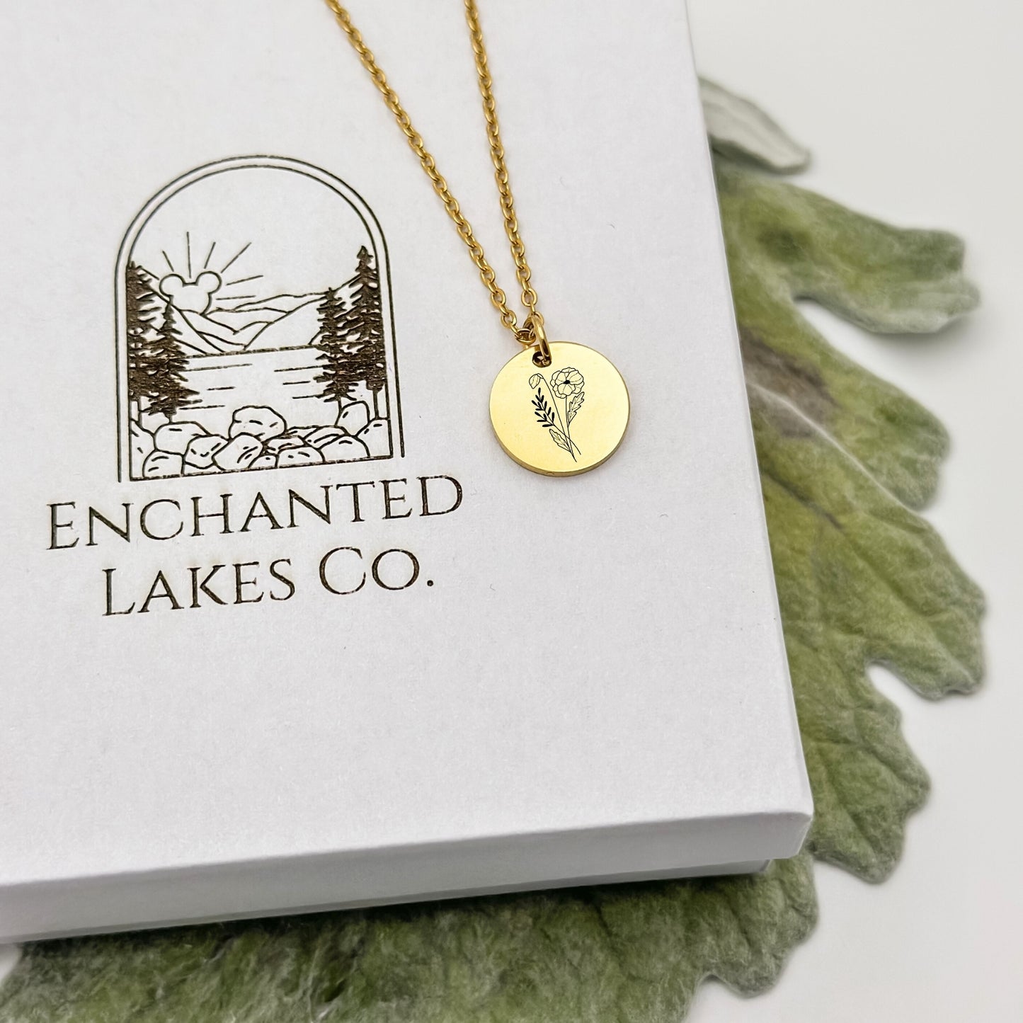 Elegant 18K PVD Gold circle charm necklace featuring a detailed poppy engraving, symbolizing August birthdays. Hypoallergenic, waterproof, and tarnish-resistant.
