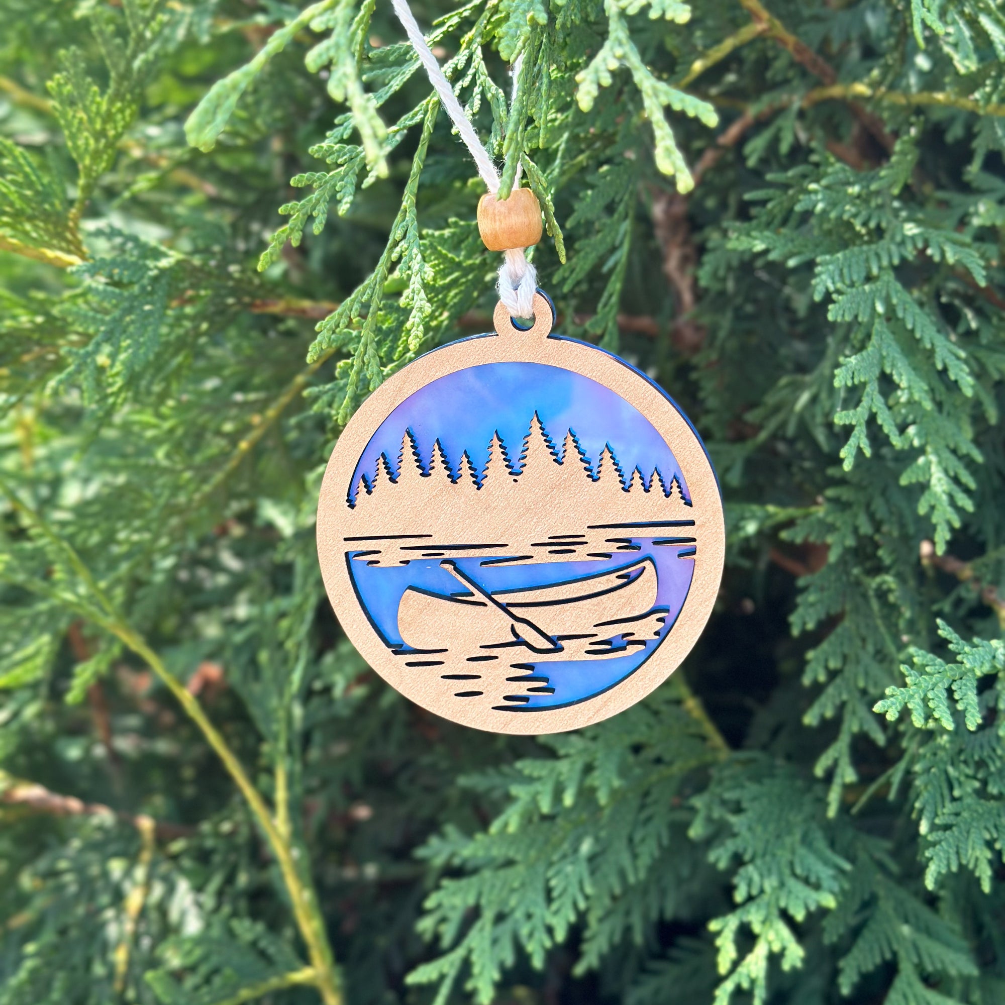 Wooden ornament with a lake and canoe design hanging on a tree.