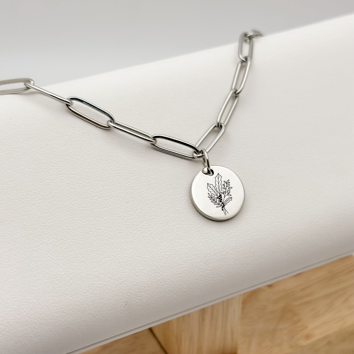 Silver circle charm necklace featuring a finely engraved holly branch, the December birth flower, on a modern paperclip chain. Hypoallergenic, waterproof, and tarnish-resistant.
