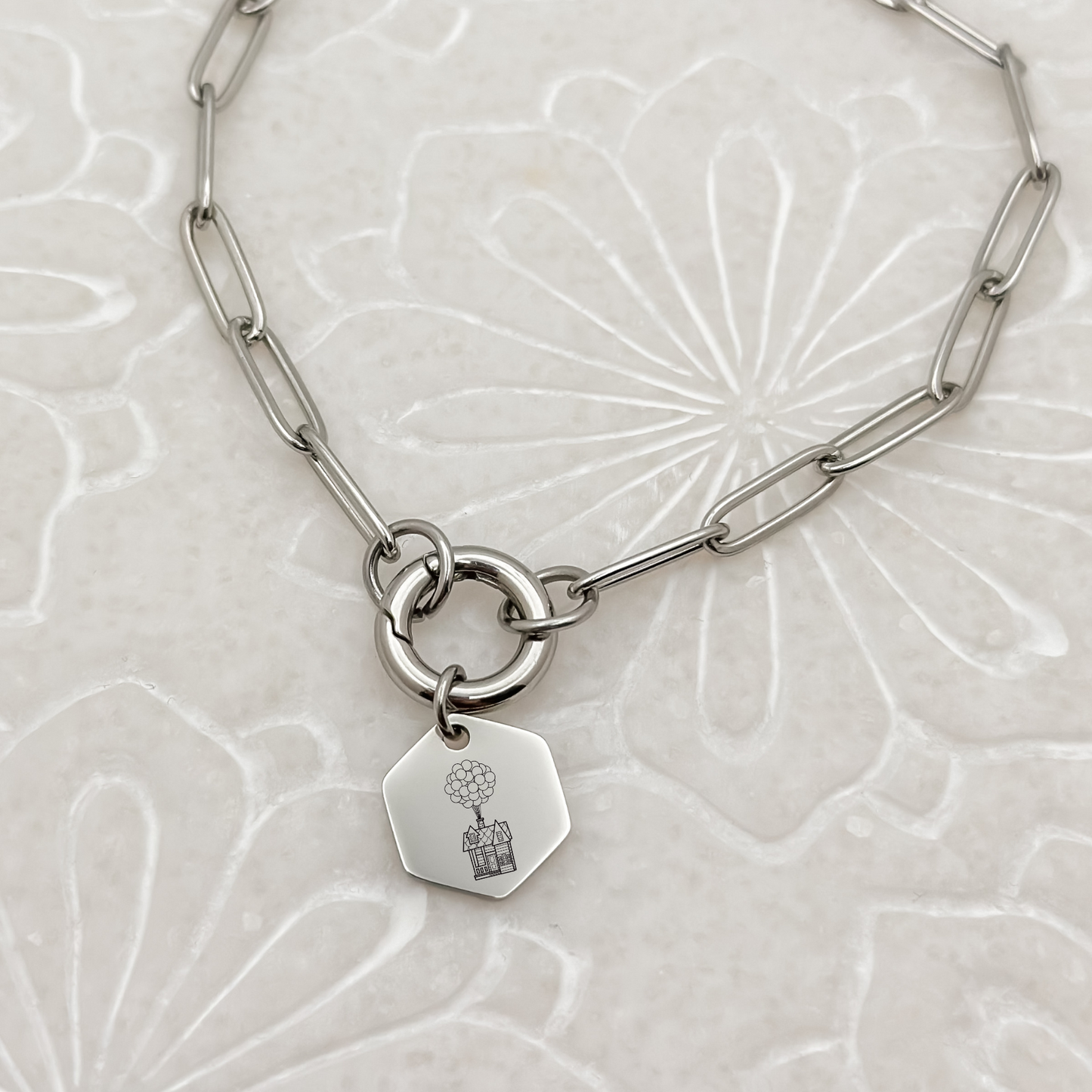 Floating House Charm Bracelet on a silver paperclip chain with charm keeper. Hexagon Charm featuring an engraved House with Balloons helping it float UP in the air. Hypoallergenic, waterproof, stainless steel jewelry.