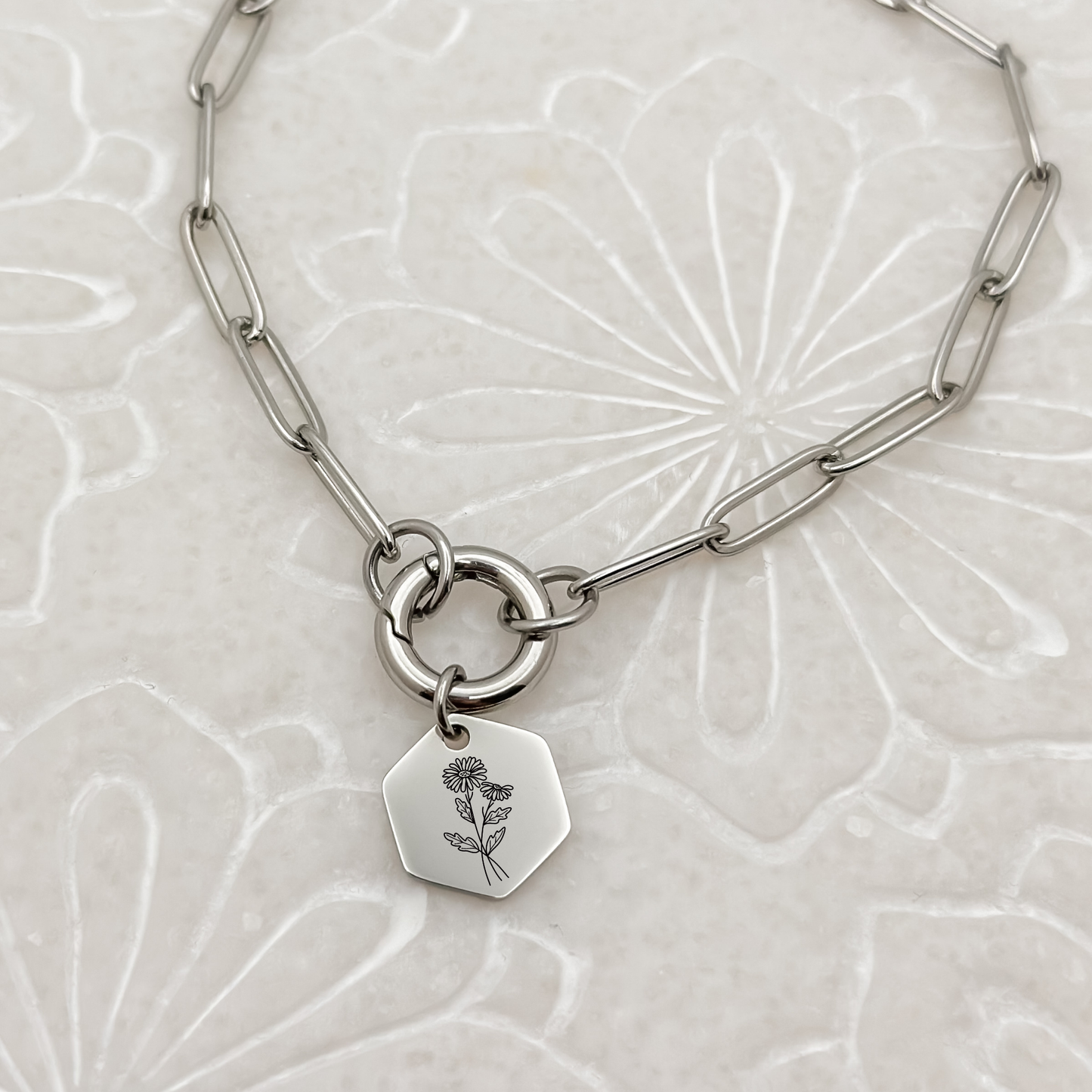 Silver hexagon charm with an engraved daisy, the April birth flower, on a charm keeper necklace. Hypoallergenic, waterproof, and tarnish-resistant.
