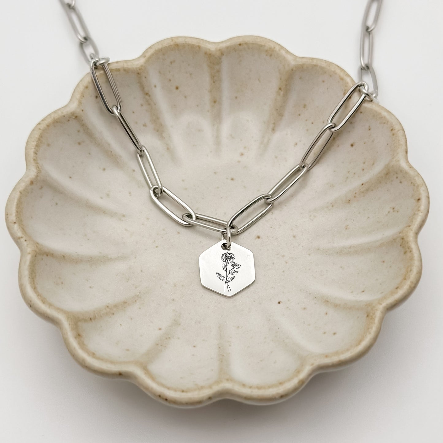Silver hexagon charm necklace engraved with a daisy, the April birth flower. A meaningful keepsake, hypoallergenic, waterproof, and tarnish-resistant.