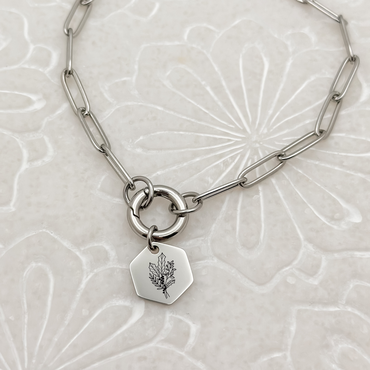Silver hexagon charm with an engraved holly branch, the December birth flower, on a charm keeper necklace. Hypoallergenic, waterproof, and tarnish-resistant.