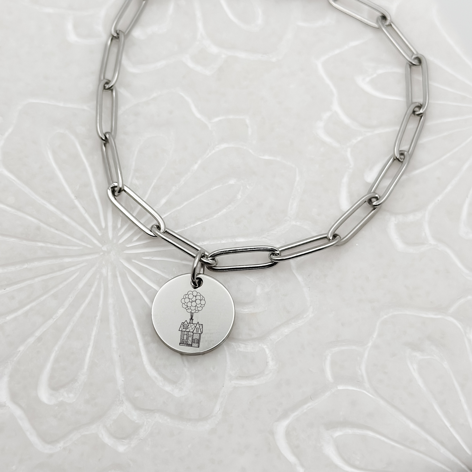 Floating House Charm Bracelet on a silver paperclip chain. Circle Charm featuring an engraved House with Balloons helping it float UP in the air. Hypoallergenic, waterproof, stainless steel jewelry.