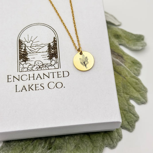 Elegant 18K PVD Gold circle charm necklace featuring a detailed holly branch engraving, symbolizing December birthdays. Hypoallergenic, waterproof, and tarnish-resistant.