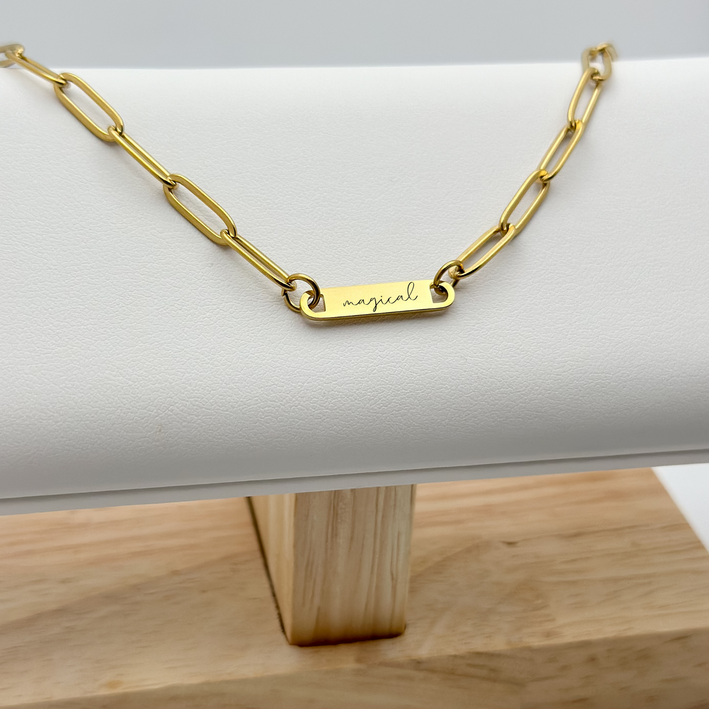 Detailed close-up of the gold bar necklace with "magical" engraving, showcasing its polished finish and delicate chain.