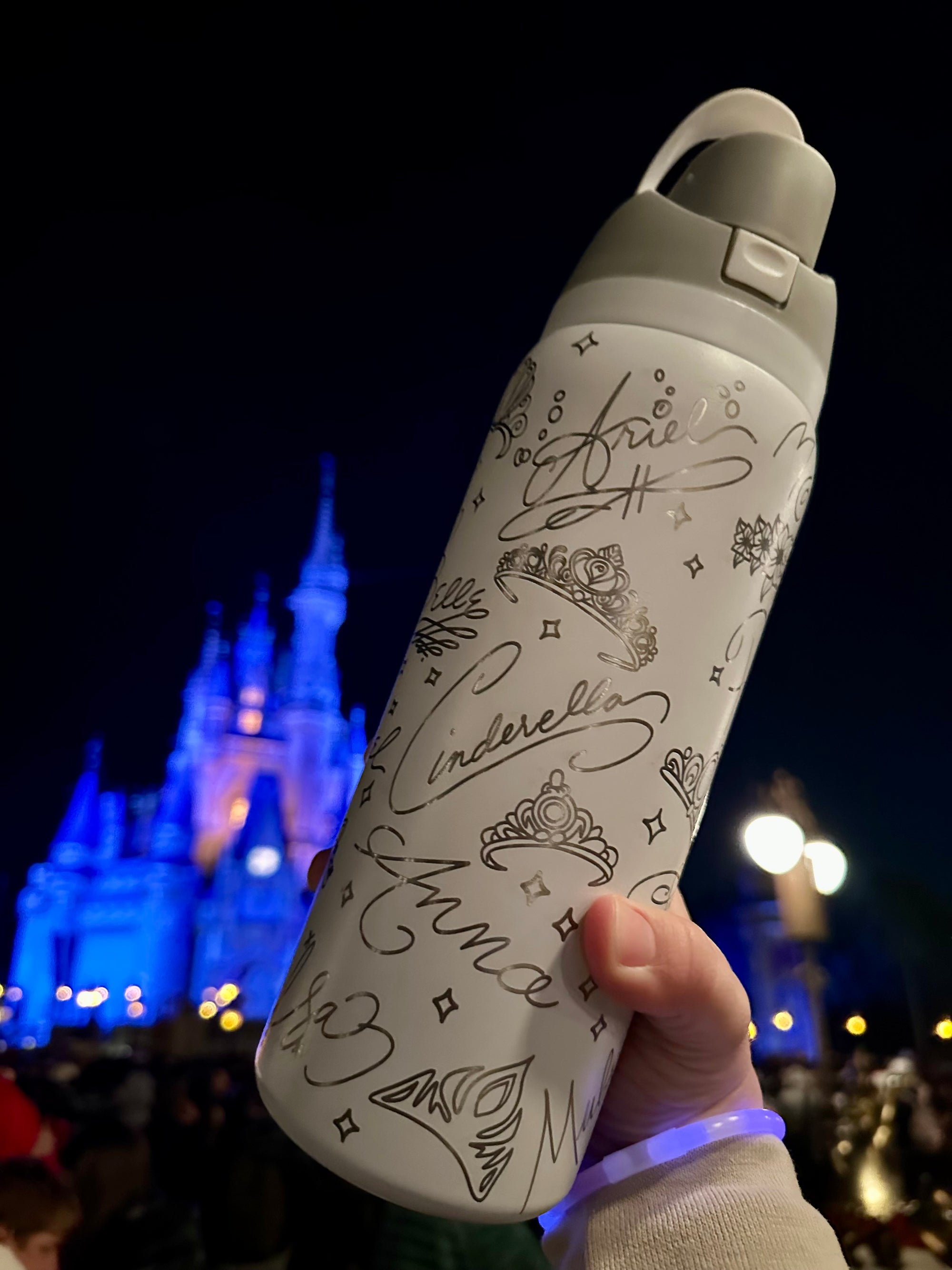 White water bottle with black designs held in front of a castle at night