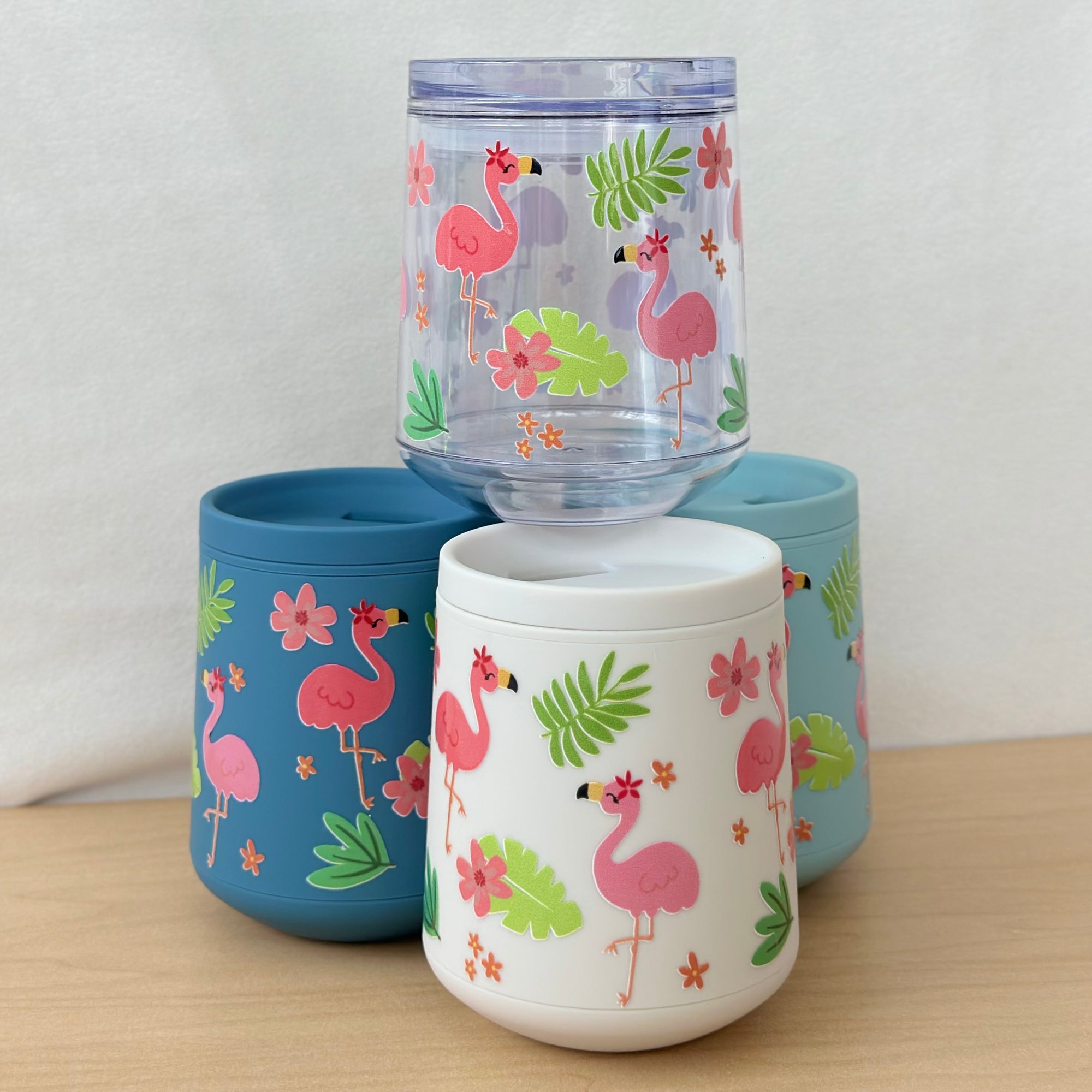 Set of three colorful tumblers with flamingo design on a wooden surface.