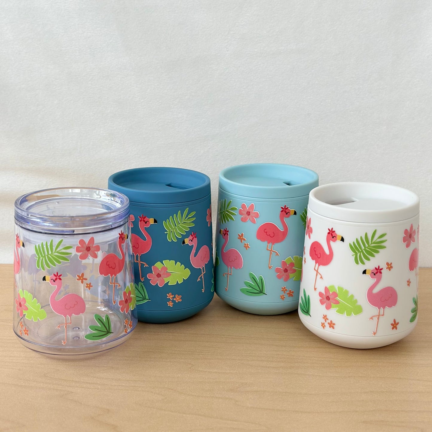 Four colorful tumblers with flamingo designs on a wooden surface.