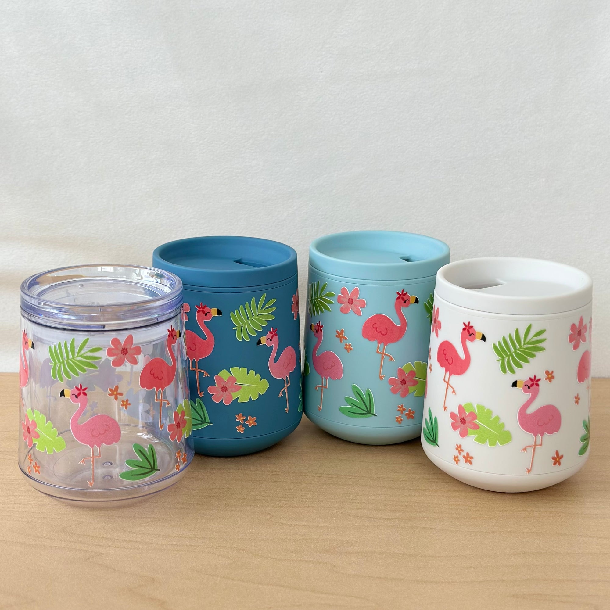 Four colorful tumblers with flamingo designs on a wooden surface.
