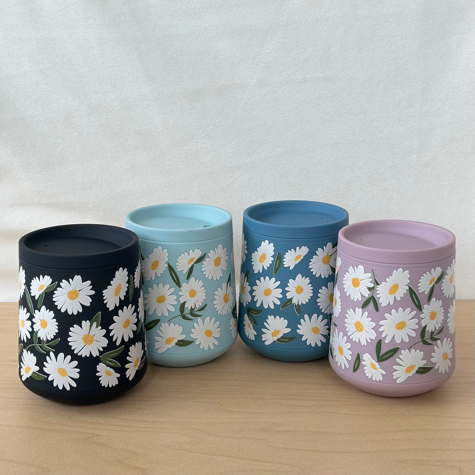 Four tumblers with daisy patterns on a wooden surface and light gray background