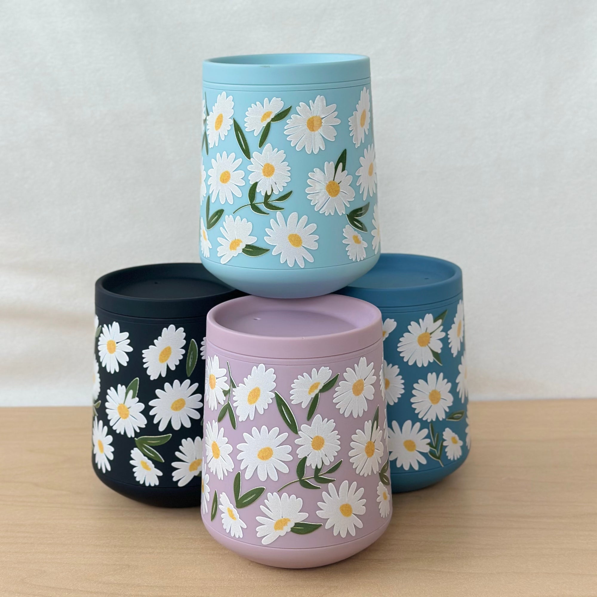 Four cylindrical containers with daisy pattern on a wooden surface