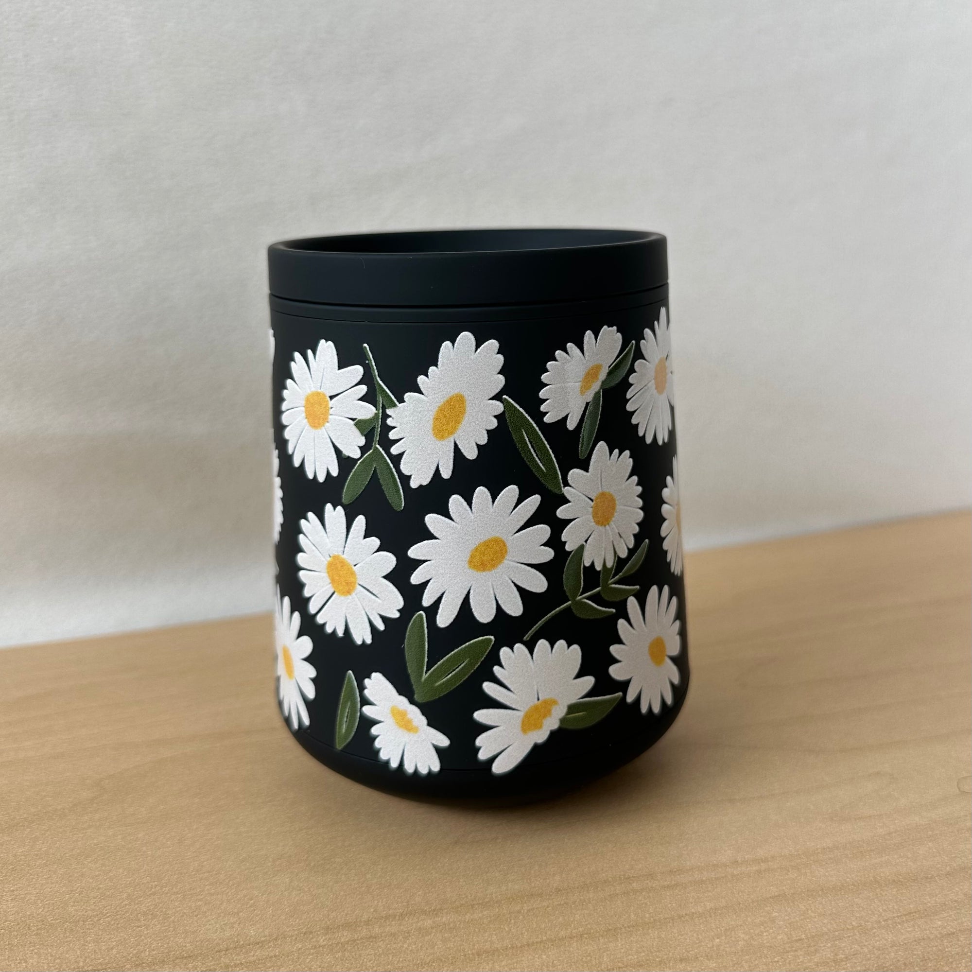 Black tumbler with white daisy pattern on a wooden surface