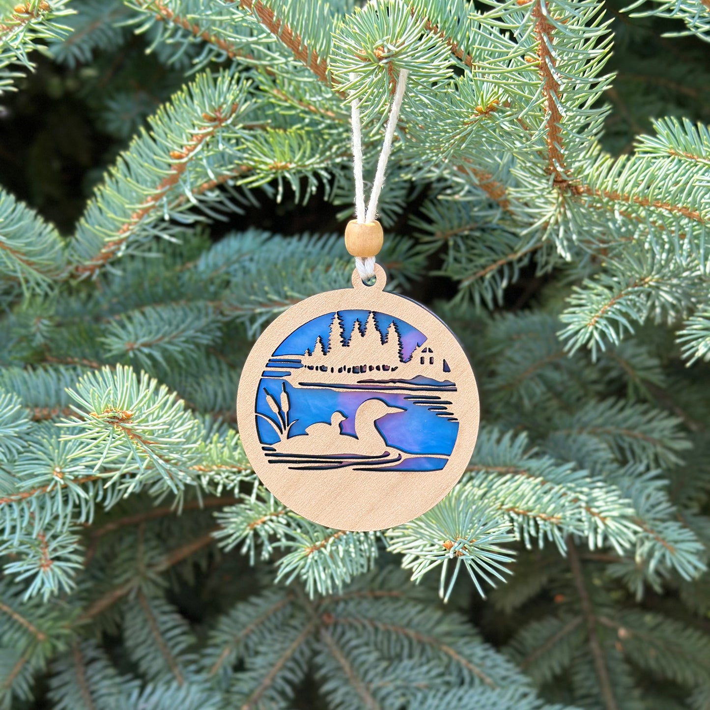 Decorative ornament with a landscape design hanging on a Christmas tree.