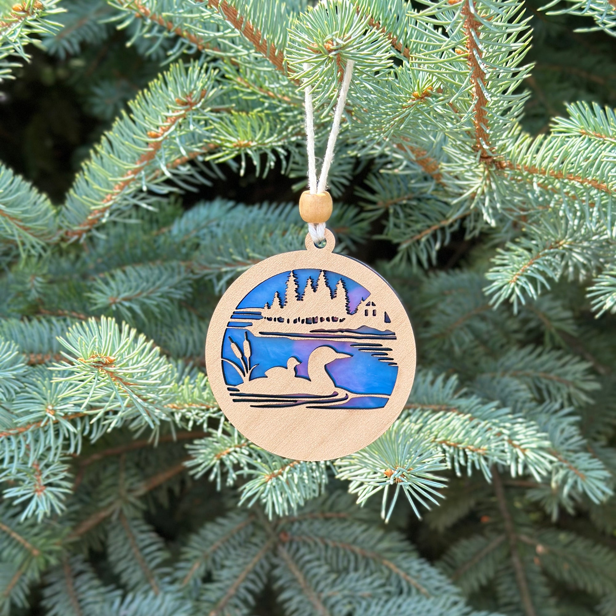 Decorative ornament with a landscape design hanging on a Christmas tree.