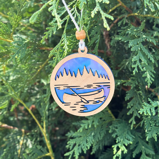 Wooden ornament with a lake and canoe design hanging on a tree.