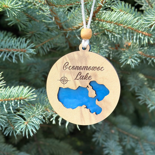 Wooden ornament with blue map and 'Oconomowoc Lake' text, hanging on a tree.