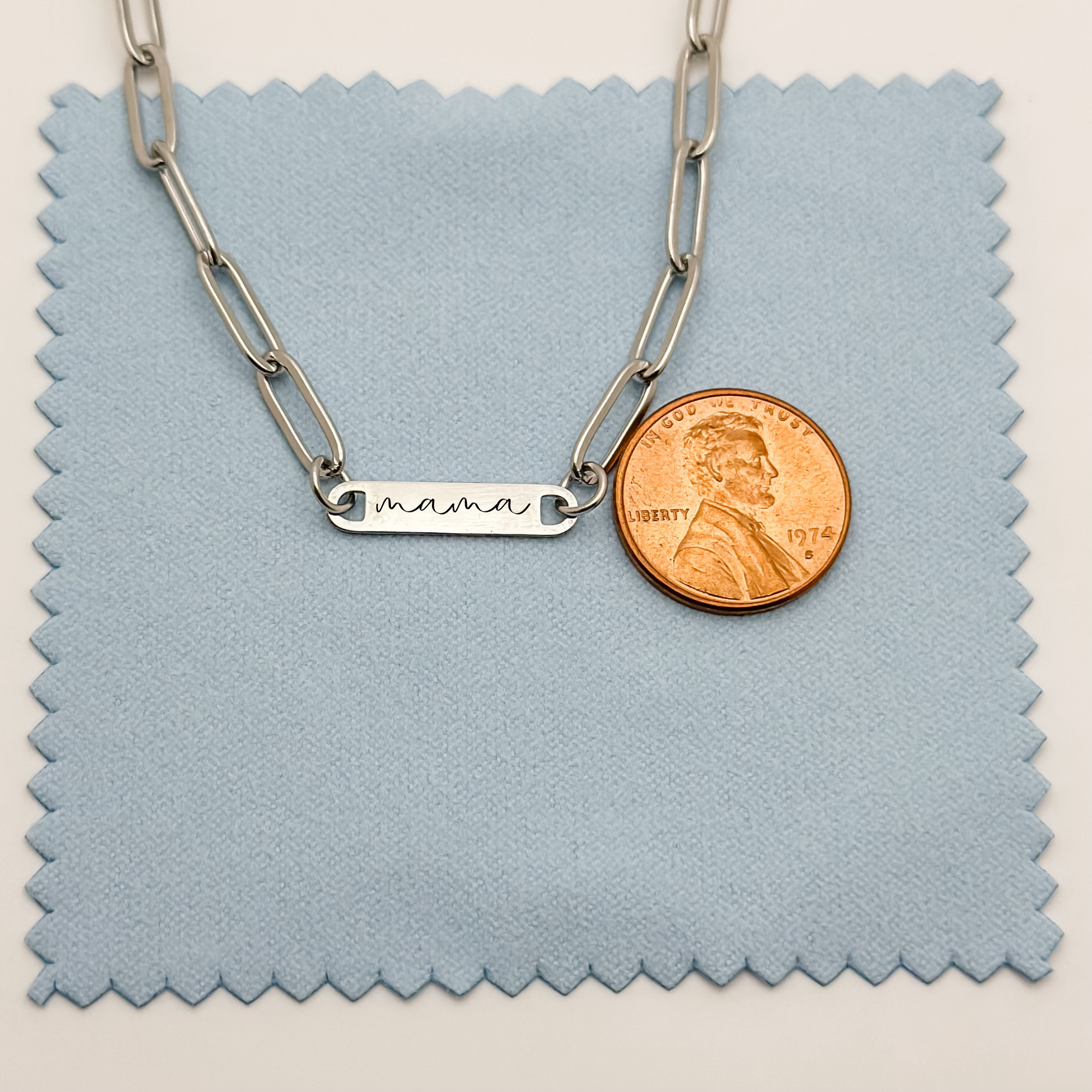 A size comparison of the engraved "mama" bar necklace in silver, placed next to a penny to showcase its delicate proportions.