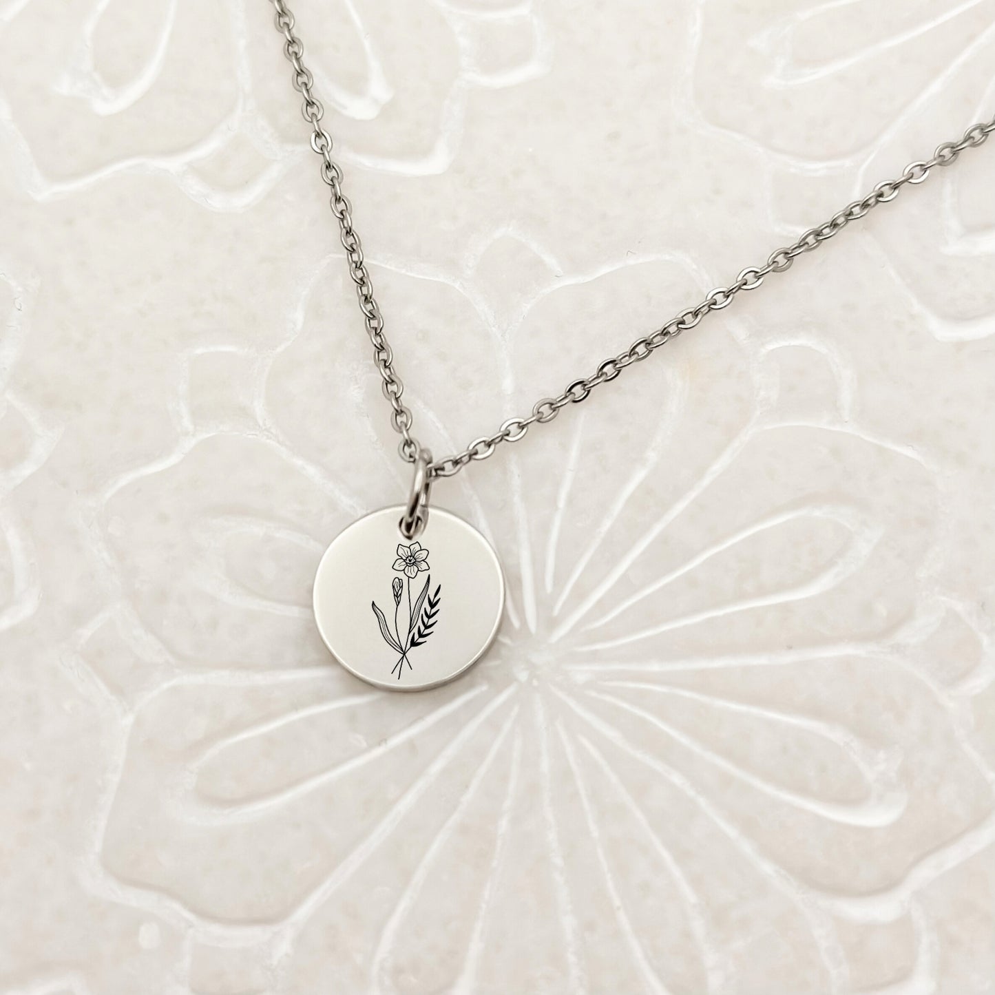 Minimalist silver circle charm necklace with a beautifully engraved daffodil, the March birthflower. Hypoallergenic, waterproof, and tarnish-resistant.