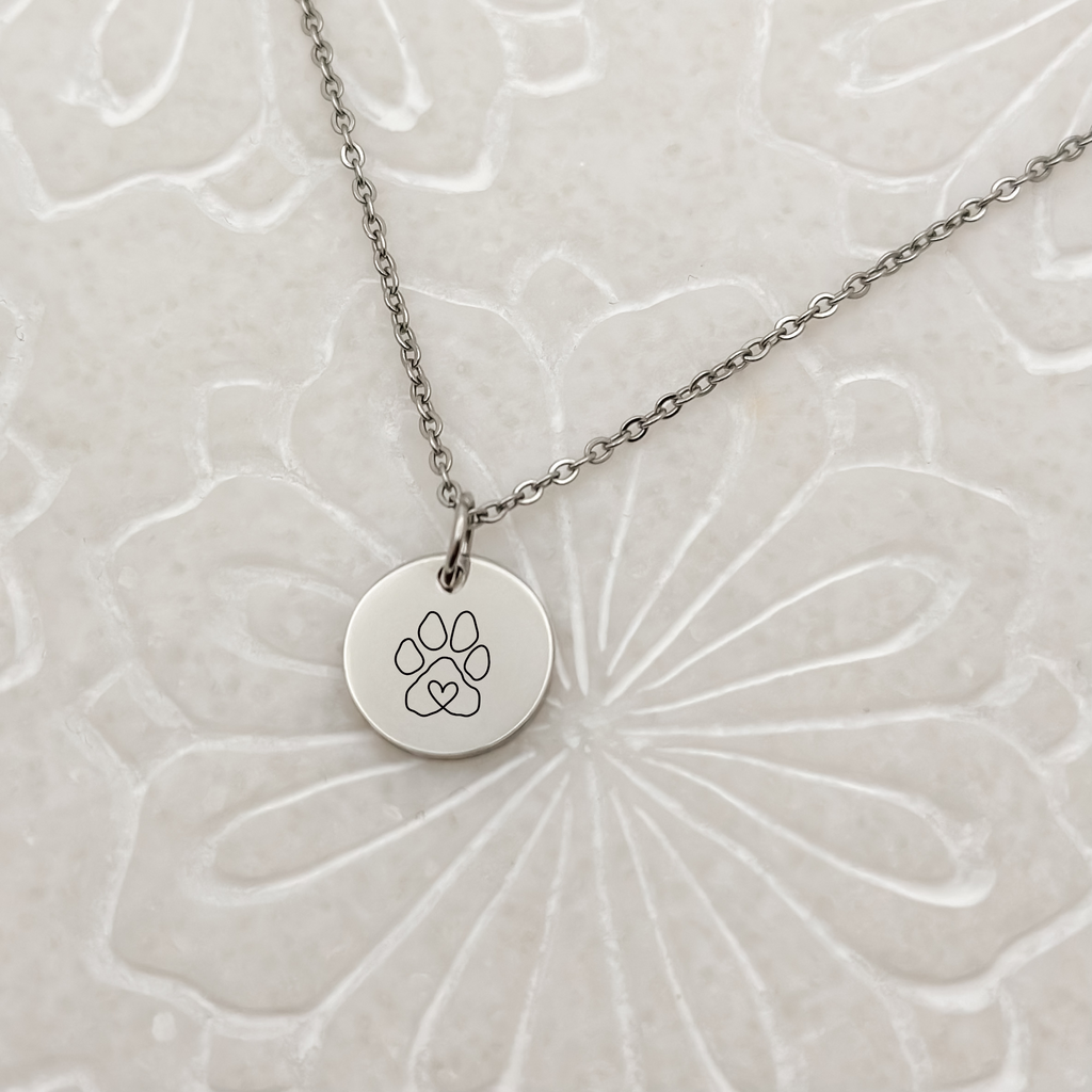 Elegant silver circle charm with a minimalist paw print on a classic loop chain necklace. Hypoallergenic, waterproof, and tarnish-resistant—perfect for pet lovers.