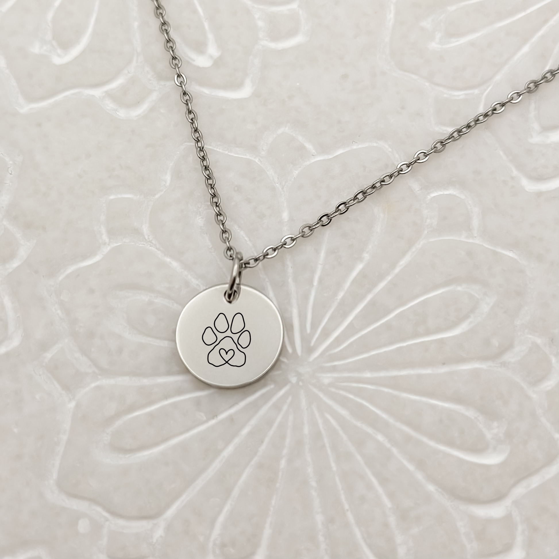 Elegant silver circle charm with a minimalist paw print on a classic loop chain necklace. Hypoallergenic, waterproof, and tarnish-resistant—perfect for pet lovers.