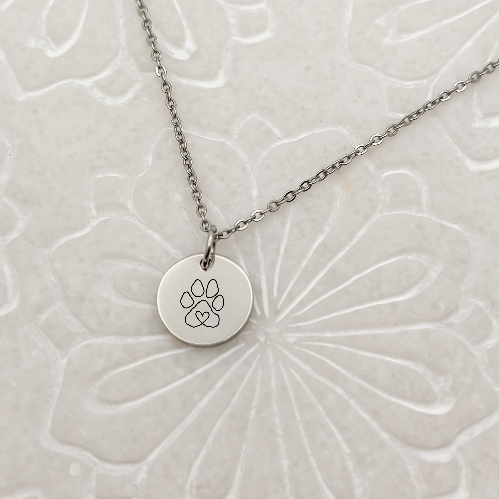 Elegant silver circle charm with a minimalist paw print on a classic loop chain necklace. Hypoallergenic, waterproof, and tarnish-resistant—perfect for pet lovers.