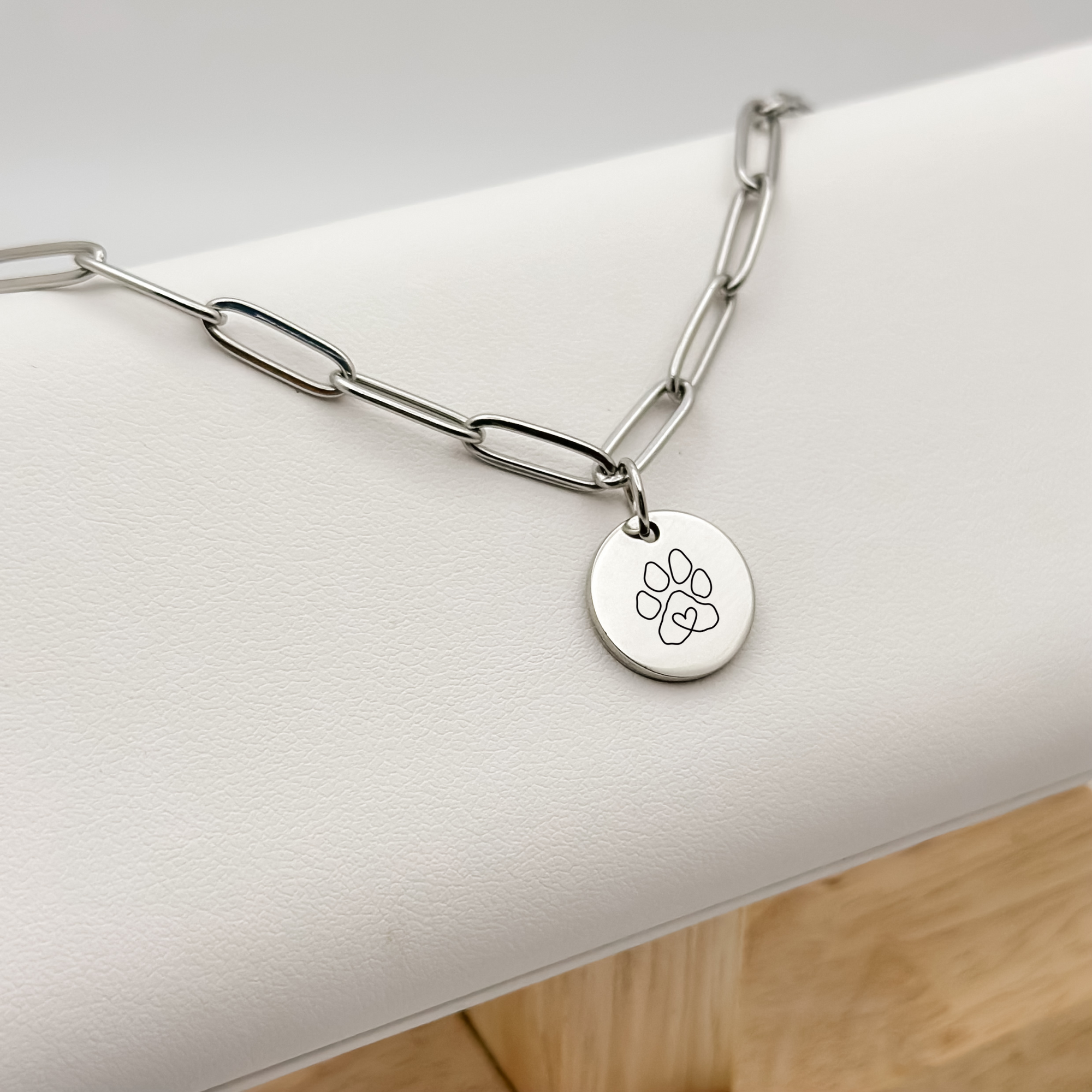 Silver circle charm necklace with a dainty paw print design on a stylish paperclip chain. Made from hypoallergenic, waterproof, and tarnish-resistant stainless steel, perfect for pet lovers.