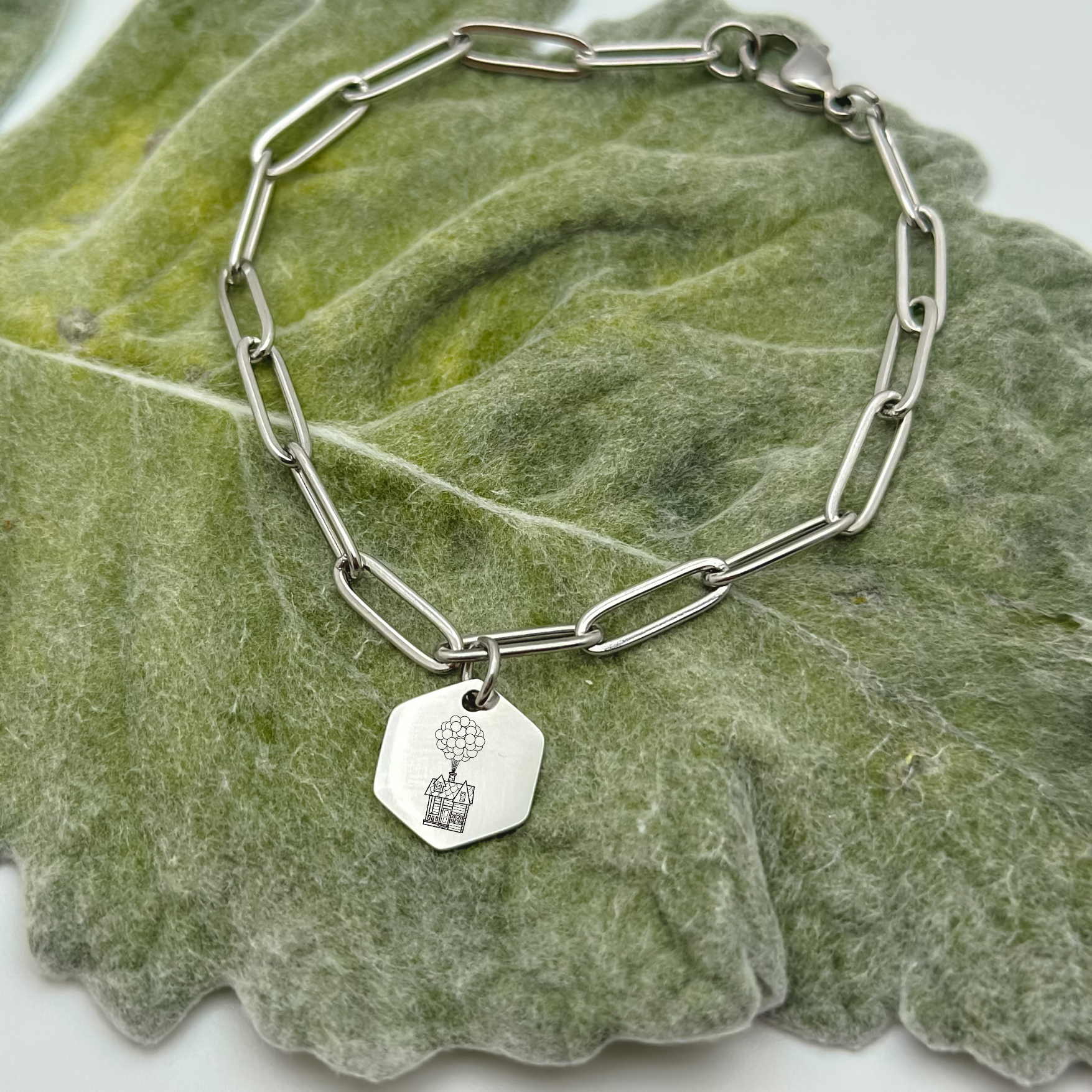 Floating House Charm Bracelet on a silver paperclip chain. Hexagon Charm featuring an engraved House with Balloons helping it float UP in the air. Hypoallergenic, waterproof, stainless steel jewelry.