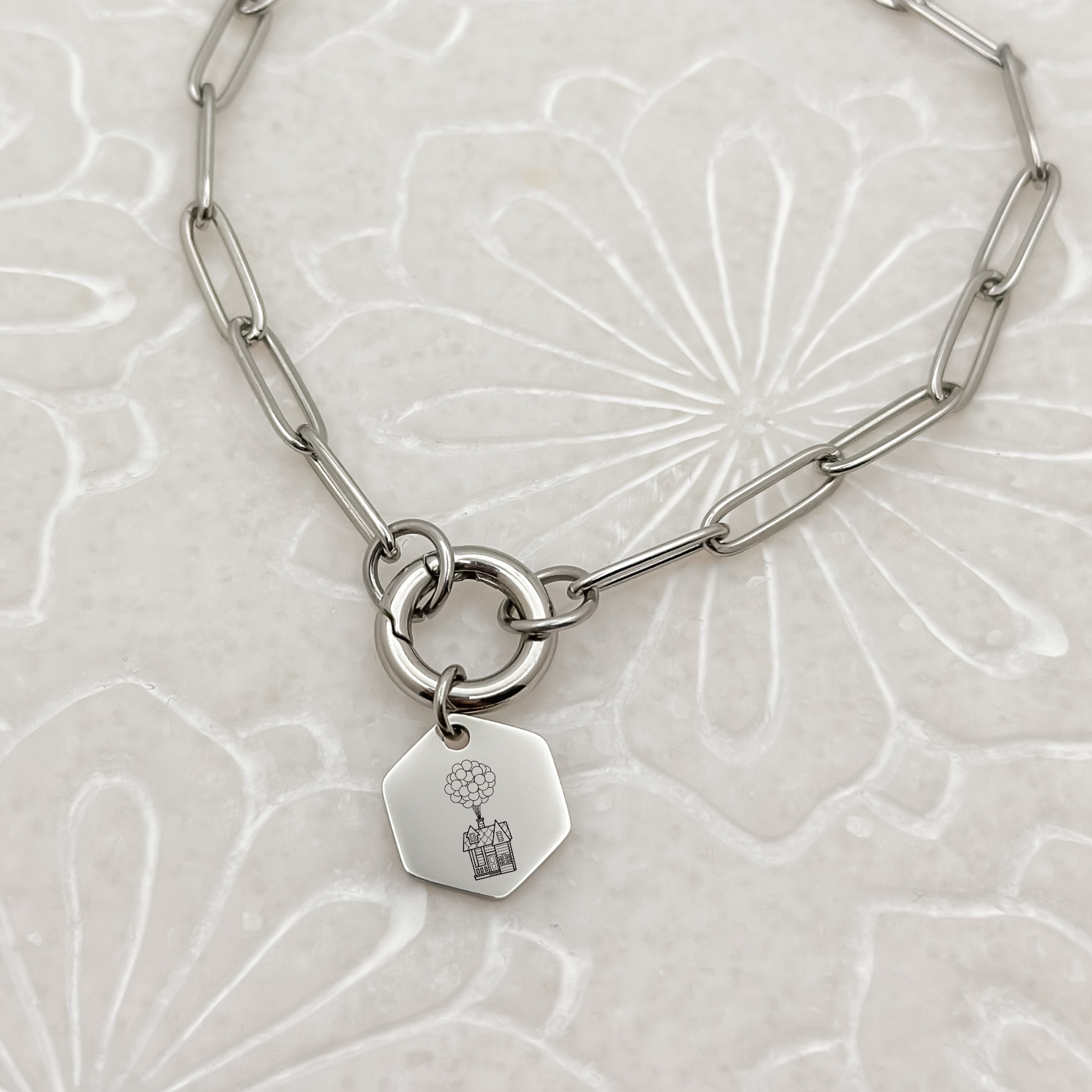Floating House Charm Bracelet on a silver paperclip chain with charm keeper. Hexagon Charm featuring an engraved House with Balloons helping it float UP in the air. Hypoallergenic, waterproof, stainless steel jewelry.