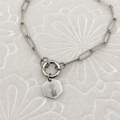 Floating House Charm Bracelet on a silver paperclip chain with charm keeper. Hexagon Charm featuring an engraved House with Balloons helping it float UP in the air. Hypoallergenic, waterproof, stainless steel jewelry.