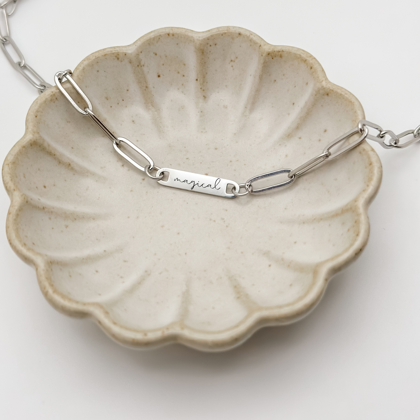 A close-up of the silver "magical" bar necklace, highlighting the elegant engraving and stainless steel craftsmanship.