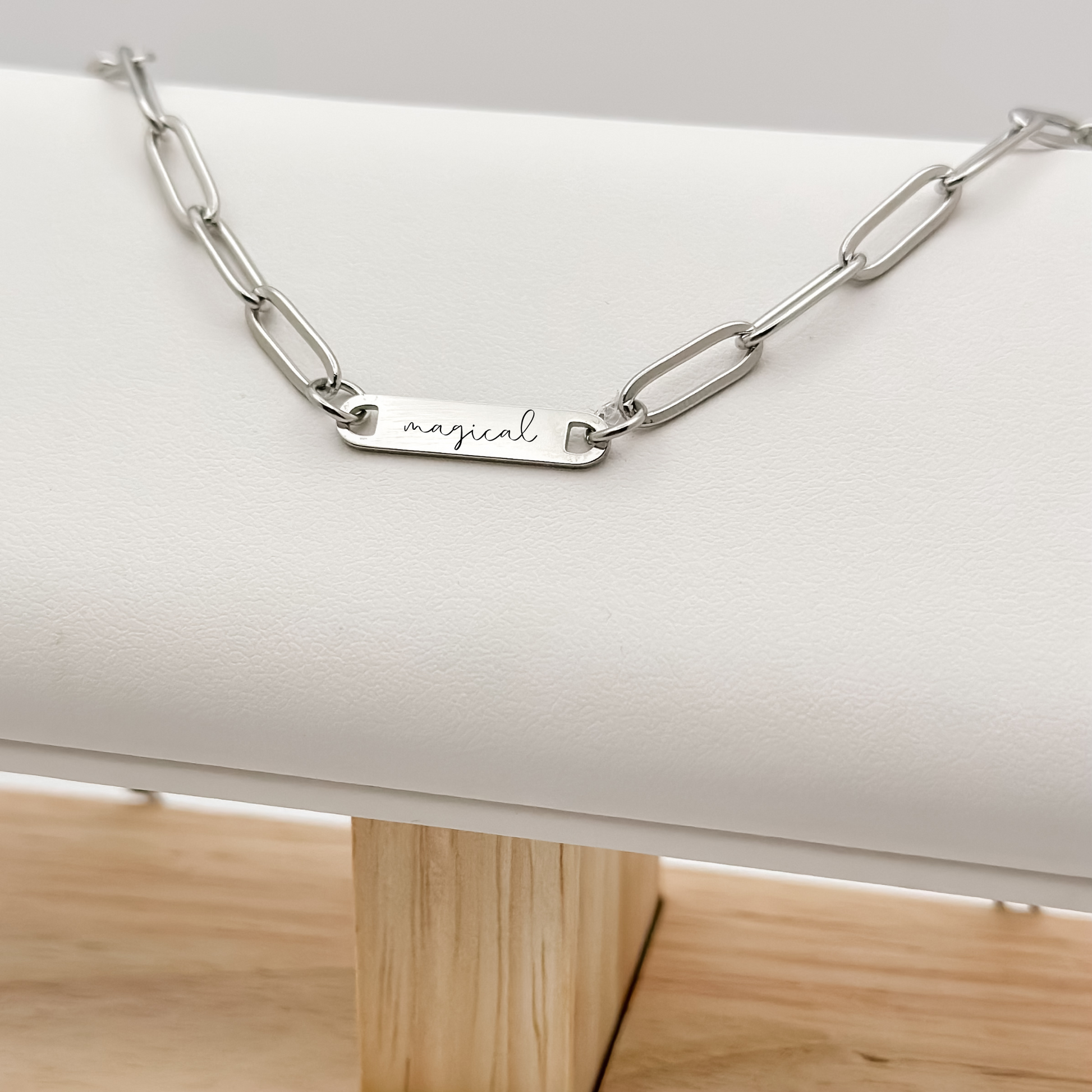 A sleek silver bar necklace engraved with "magical," featuring a modern paperclip chain for everyday elegance