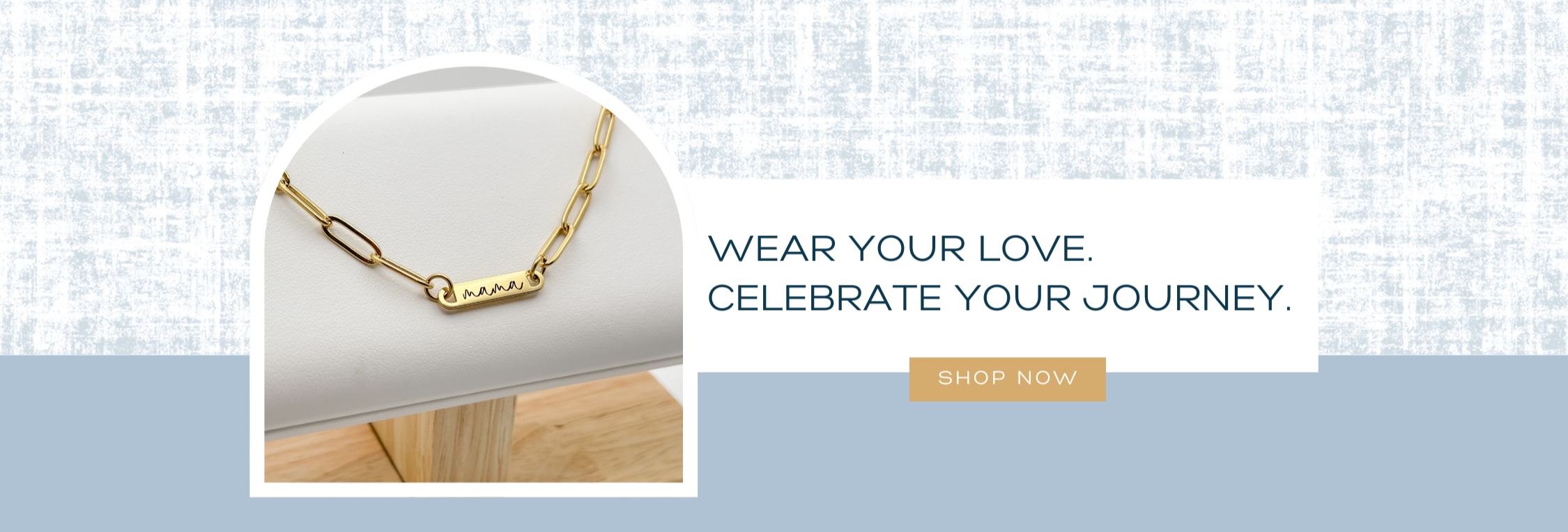 Gold necklace on a white stand with a light blue background and text 'Wear your love, celebrate your journey.'