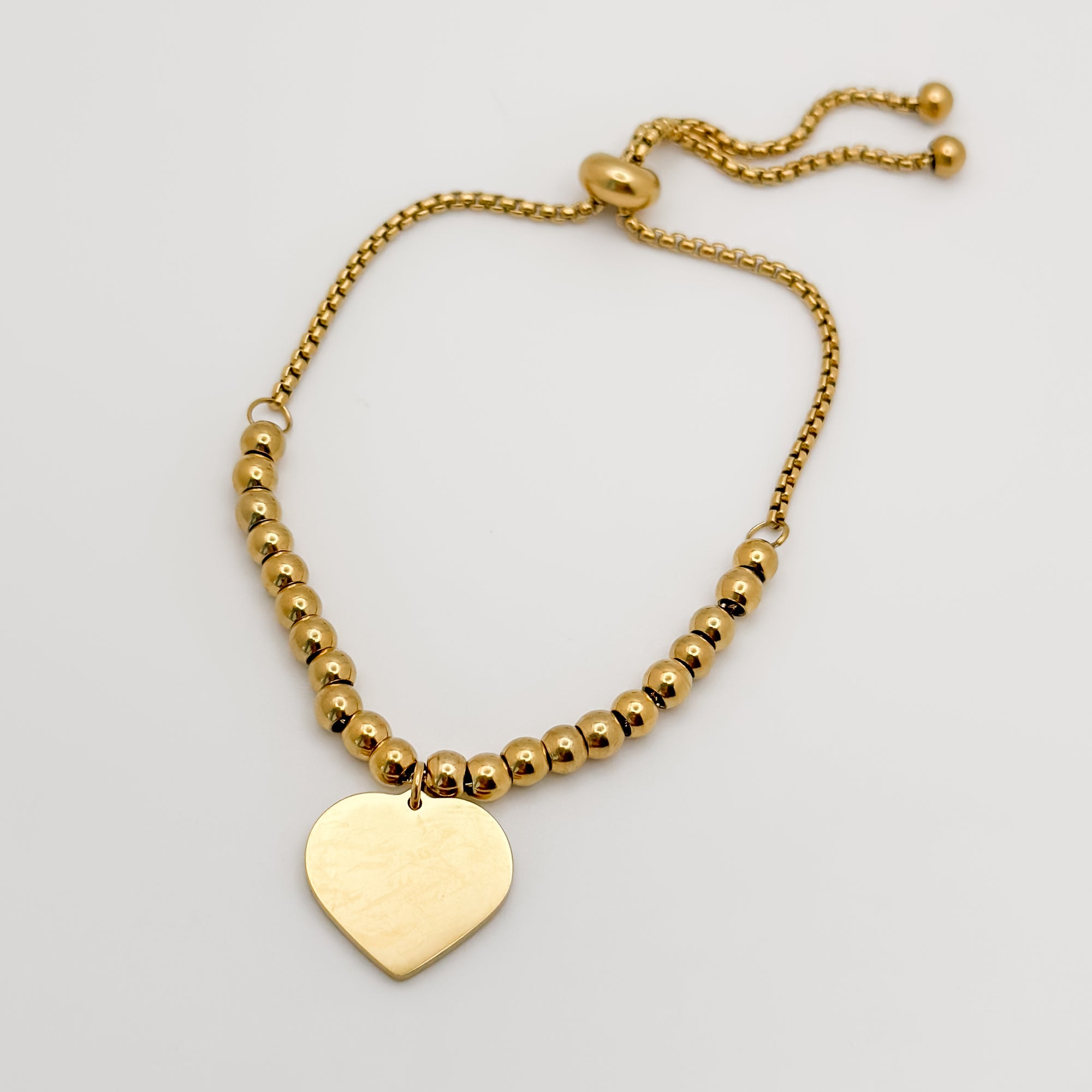 Gold beaded bracelet with a heart-shaped tag on a light gray background
