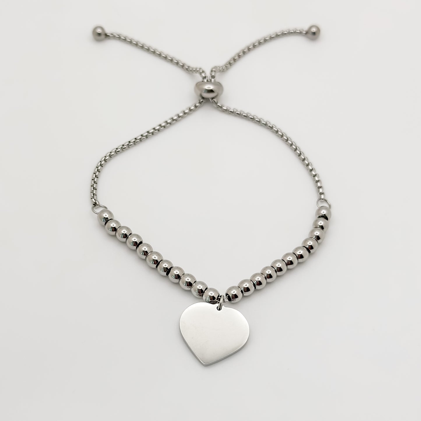 Silver beaded bracelet with a heart-shaped pendant on a light gray background